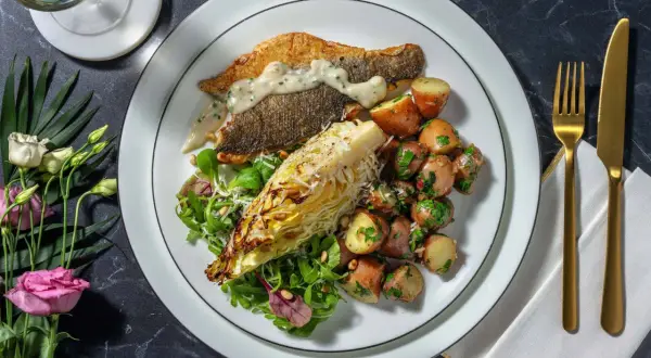 En tallrik med havsabborre, rostade potatisar, sallad och en bit grillad kål. Ett perfekt havsabborre recept för en fin middag.