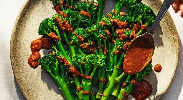 Ånga broccoli med en kryddig sås. En sked häller över mer sås på de gröna buketterna.