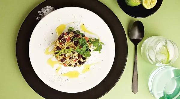 En portion gallo pinto med ris och svarta bönor, garnerad med koriander och en oljedressing. Serveras med limeklyftor och en drink med is.