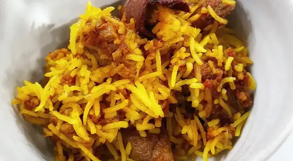En skål med gyllene ris och möra bitar av lammkött. En härlig lamm biryani som ser otroligt god ut.