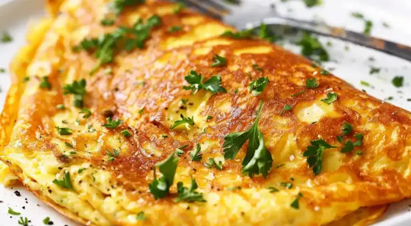 En gyllene omelett, perfekt för ett snabbt omelett recept. Garnerad med färsk persilja och serverad på en vit tallrik med en gaffel.