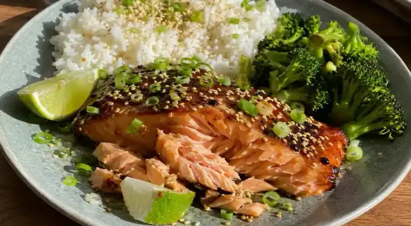 En läcker tallrik med asiatisk lax i ugn, serverad med ris, broccoli och limeklyftor.
