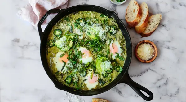 Grön shakshuka med ägg, avokado och jalapeño i gjutjärnspanna. Perfekt för ett smakrikt shakshuka recept.
