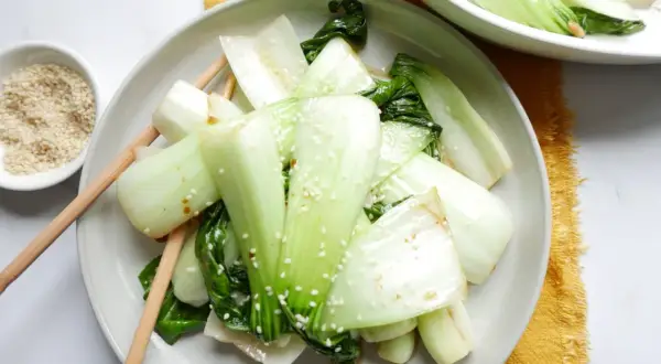 Enkel pak choi recept med sesamfrön. Grönsakerna är serverade på en tallrik med ätpinnar.