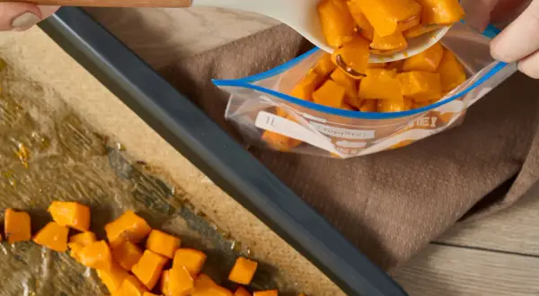 Förbereder butternutpumpa för ett recept. Tärnad pumpa läggs från en sked till en fryspåse.