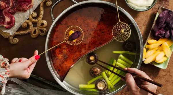 En person lägger ner grönsaker i en hot pot med två olika buljonger. Ett perfekt hot pot recept för en mysig kväll.