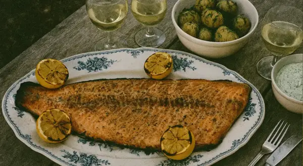 En stor grillad laxsida med citronklyftor på ett vackert fat. Serveras med dillpotatis, vit sås och vitt vin.