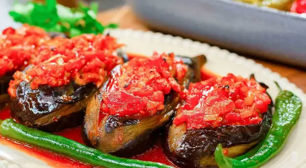 Tre auberginehalvor fyllda med tomat och paprika, serverade med gröna chilis. En härlig imam bayildi.