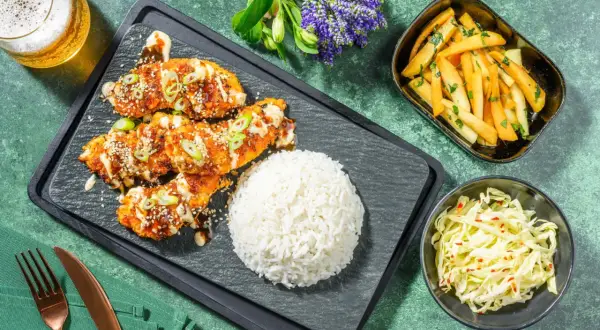 Krispig koreansk kyckling med sesamfrön och salladslök, serverad med ris, pommes frites och kålsallad.
