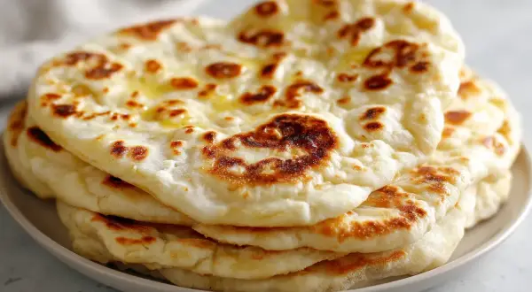 En stapel fluffigt, gyllene naanbröd, perfekt för ditt nästa naan recept. Smält smör glänser på toppen.