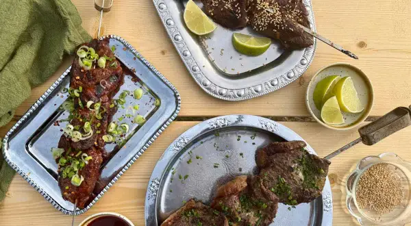 Grillad koreansk råbiff på spett, toppad med salladslök och chiliflakes. Serveras med limeklyftor och en skål sesamfrön.