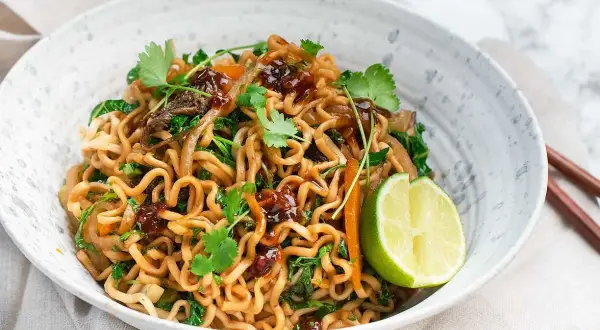 En skål med god wok med nudlar, grönsaker och en limeklyfta.