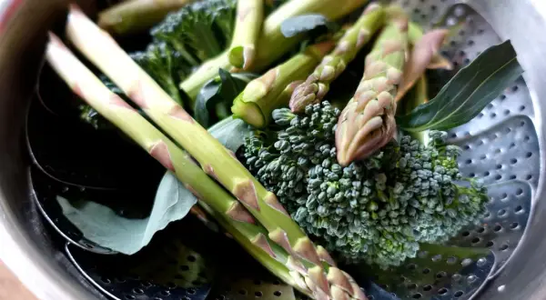 Grön sparris och broccoli ligger i en ångkorg, redo att ångkokas till perfektion.