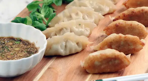 En rad gyllene, stekta dumplings och ångade dumplings serveras med en dippsås och grönsaker. Ett perfekt dumplings recept för en god måltid.