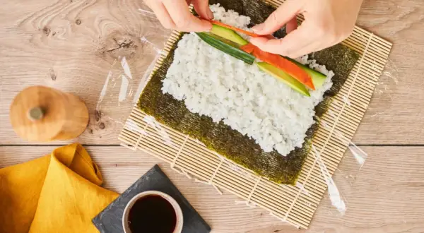 Händer lägger lax och gurka på ris för sushi maki.