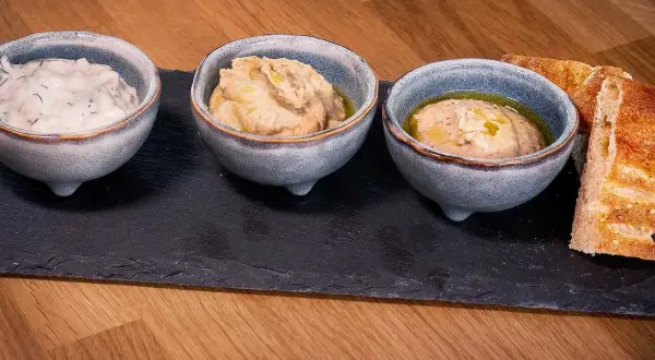Tre skålar med dippar, som tzatziki och hummus, serveras med bröd. Perfekt för ett meze recept.