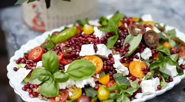 En färgglad sallad med granatäpple, tomater, fetaost och basilika, perfekt som sallad till grillat.