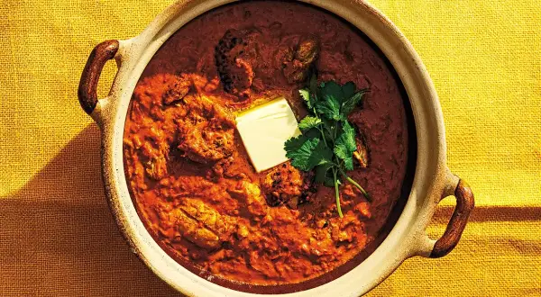 En mustig kycklingrätt i en keramikskål, toppad med en smörbit och koriander. Detta är vad "masala" betyder – en kryddblandning som ger djup och smak.