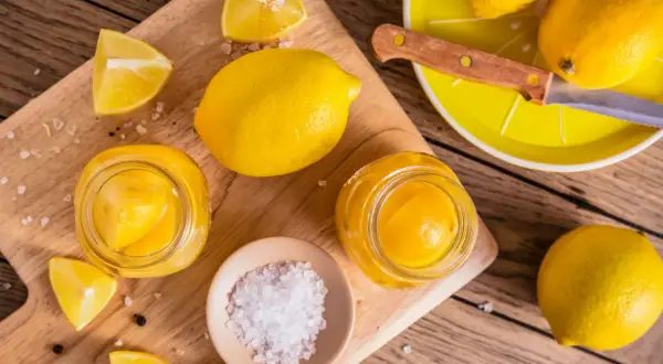 Gör ett läckert recept med inlagda citroner! Färska citroner, salt och pepparkorn förbereds på en träskärbräda.