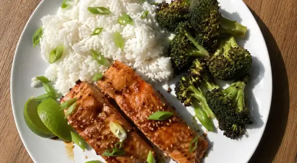 Två filéer av asiatisk lax med sesamfrön, serveras med ris, rostad broccoli och limeklyftor.