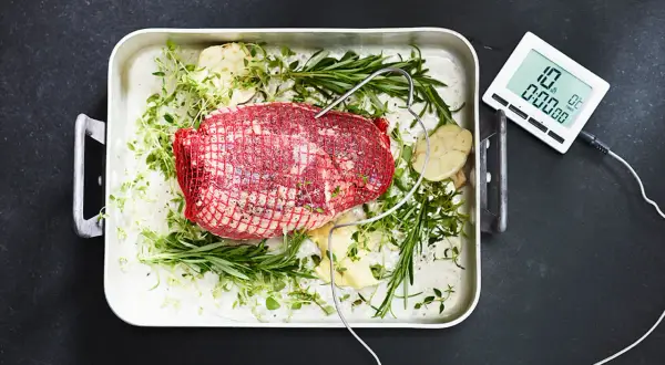 Råstek med örter och vitlök i ugnsform, redo för grillen. En digital termometer ger exakta grill tips för perfekt resultat.