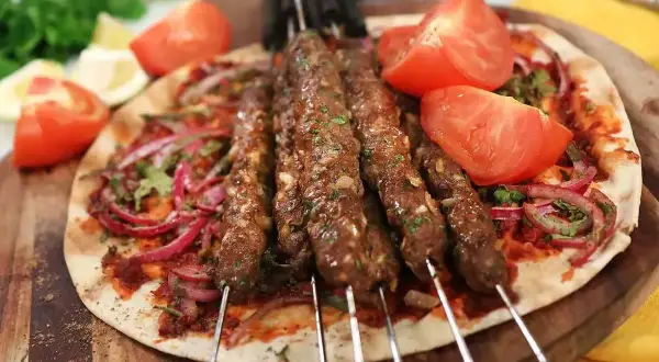 Grillad adana kebab på spett, serverad med tunnbröd, rödlök, tomat och persilja. Ett perfekt adana kebab recept för sommaren.