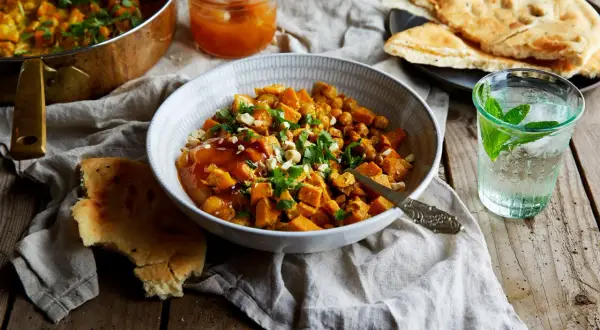 En skål med sötpotatiscurry med kikärtor, toppad med koriander och nötter. Serveras med naanbröd och en drink med mynta. Ett perfekt chilli recept.