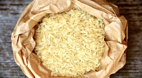 En påse med basmati eller jasminris ligger på en träyta. Riset är ljust och kornen är långa och smala.