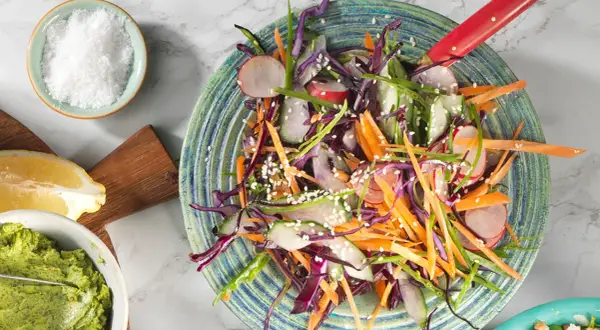 En färgglad sallad med strimlad rödkål, morot, rädisor och gurka, toppad med sesamfrön. Ett perfekt salladskål recept för en krispig och fräsch måltid.