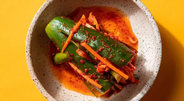 En skål med kimchi gurka, kryddad med chili och morot, på en gul bakgrund.