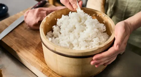 En person blandar nykokt ris i en träskål. En påminnelse om var kommer ris ifrån och hur det förbereds för sushi.