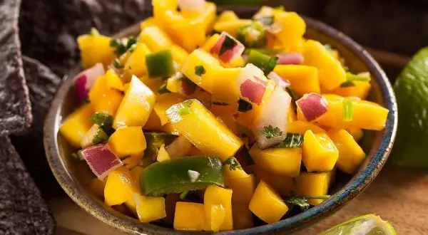 En skål med färgglad mango sallad, med tärnad mango, rödlök, grön paprika och koriander. Serveras med tortillachips och lime.