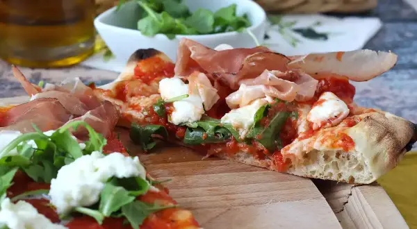 En skiva pinsa med prosciutto, mozzarella och ruccola. En härlig pinsa topping som ser utsökt ut.