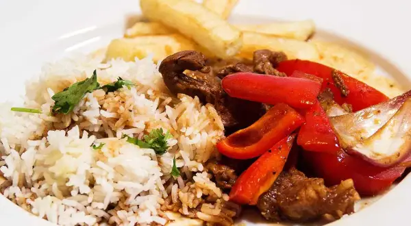 En tallrik med lomo saltado: ris, pommes frites, strimlat nötkött, rödlök och röd paprika.