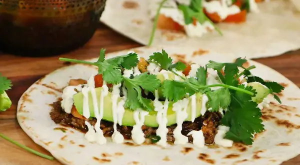 En närbild på en taco med köttfärs, avokado, koriander och en vit sås. Perfekt för ett tacokrydda recept!