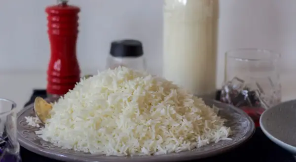 En hög med fluffigt, nykokt långkornigt ris på en tallrik. Bredvid står en röd pepparkvarn och en flaska mjölk.