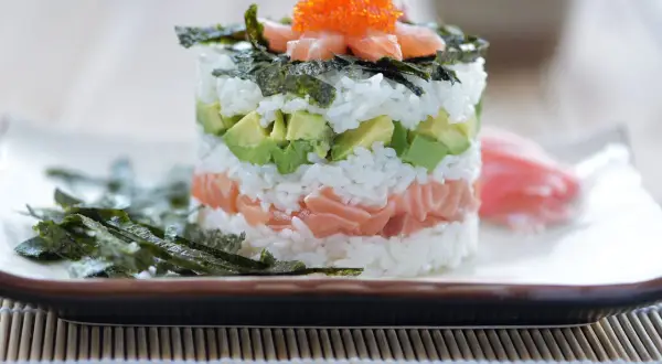 En vacker sushi tårta med lax, avokado och ris, toppad med rom och nori. En festlig rätt för alla sushiälskare.