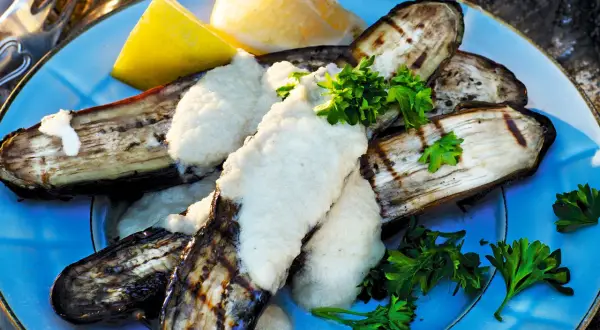 Grillad aubergine med en krämig sås och färsk persilja, serverad med citronklyftor. En härlig sommarrätt.