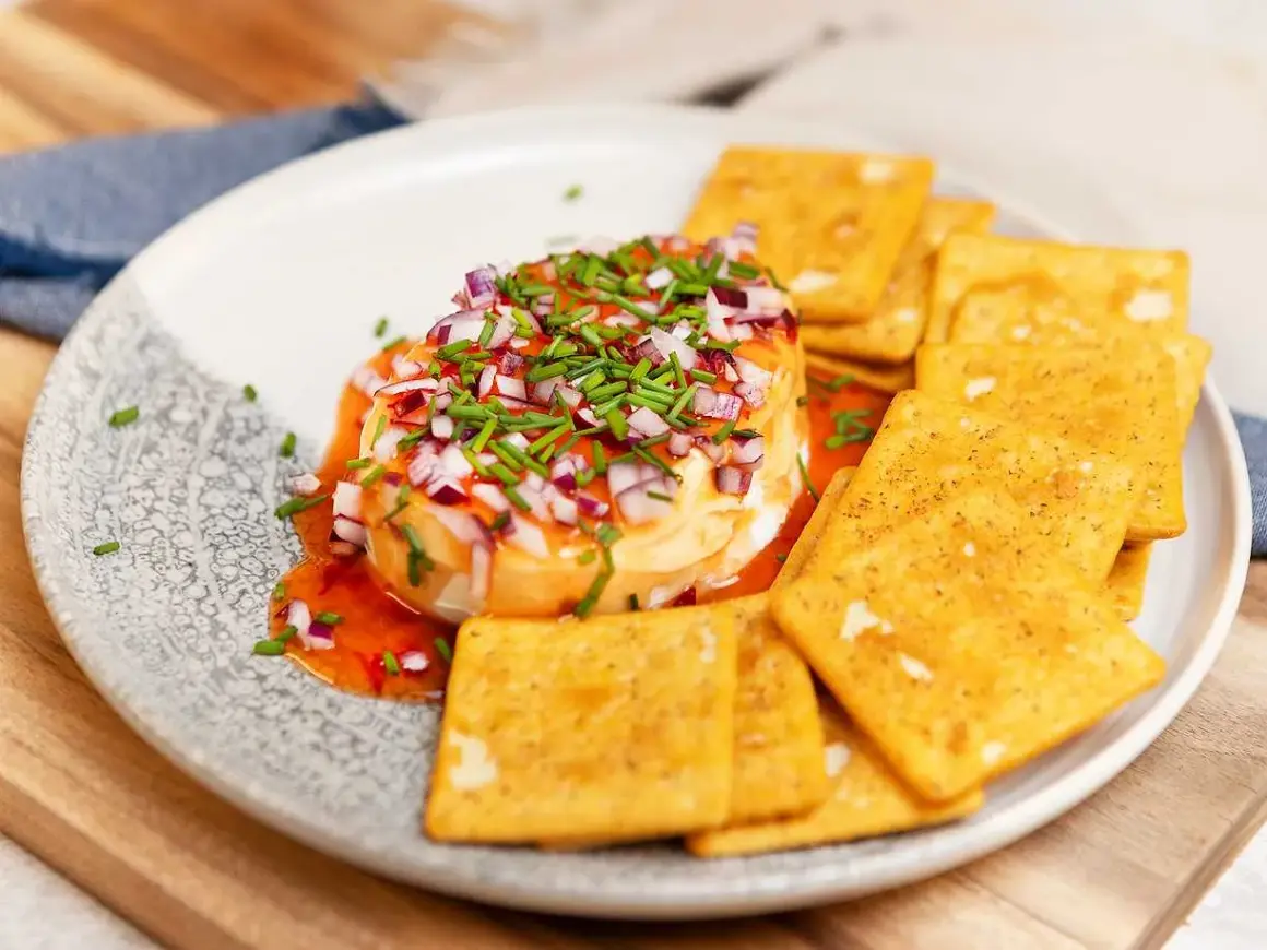 Ost med hackad rödlök och gräslök, ringlad med söt chilisås. Serveras med kex.