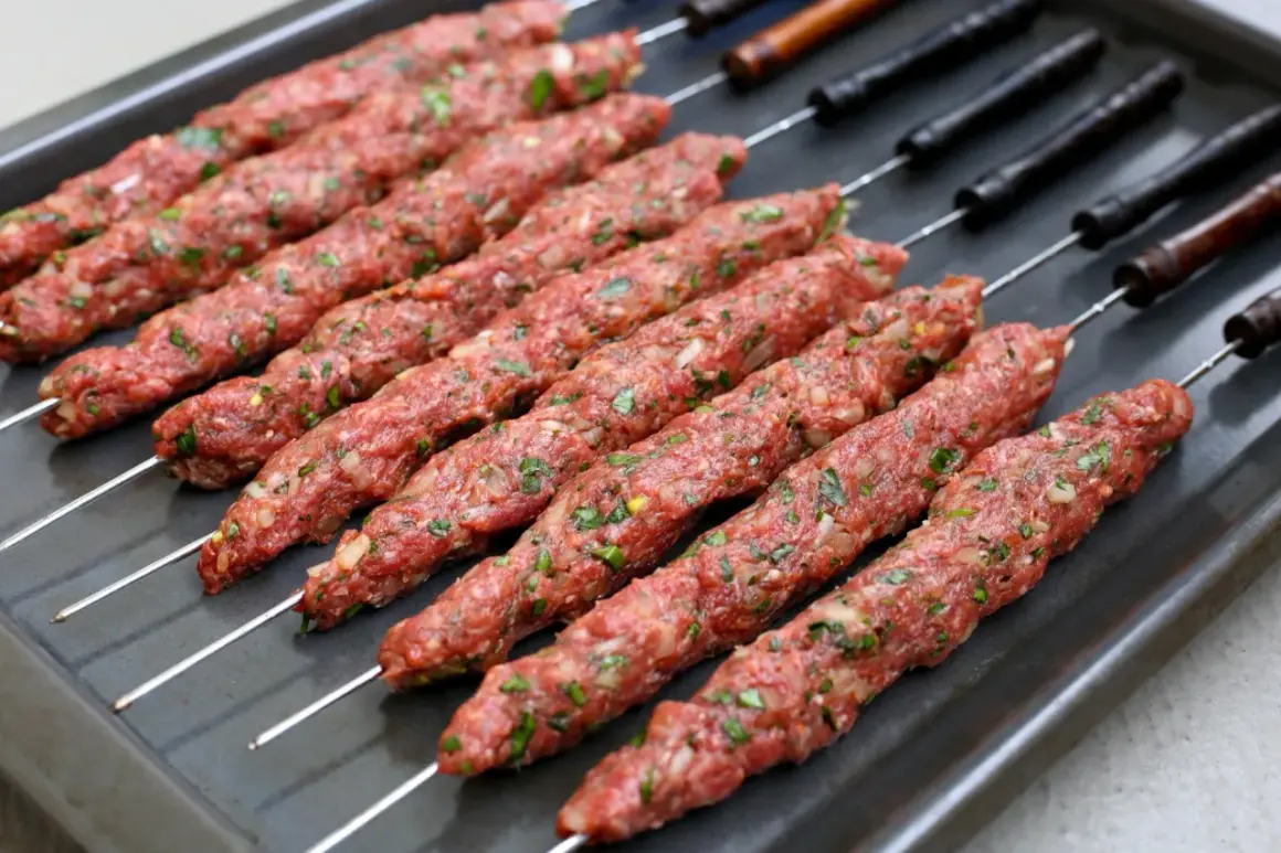 Råa kebabspett med lök och persilja ligger redo på en plåt för att tillagas i ugn.