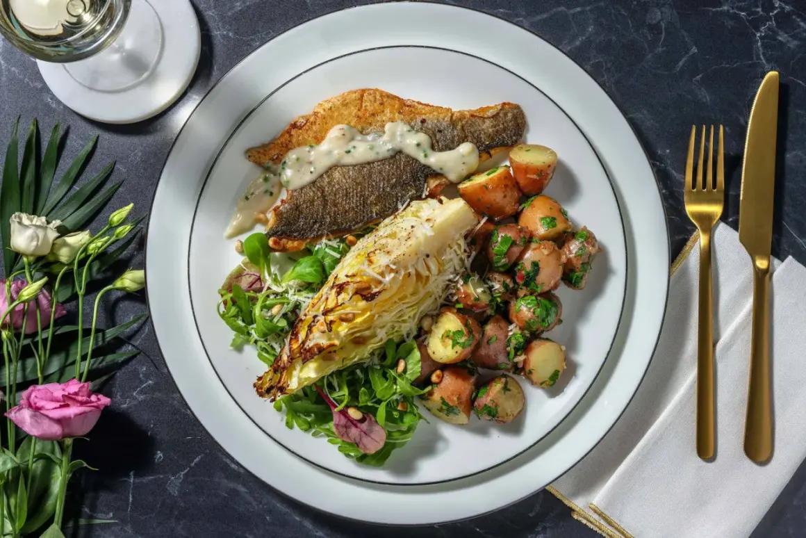 En tallrik med havsabborre, rostade potatisar, sallad och en bit grillad kål. Ett perfekt havsabborre recept för en fin middag.