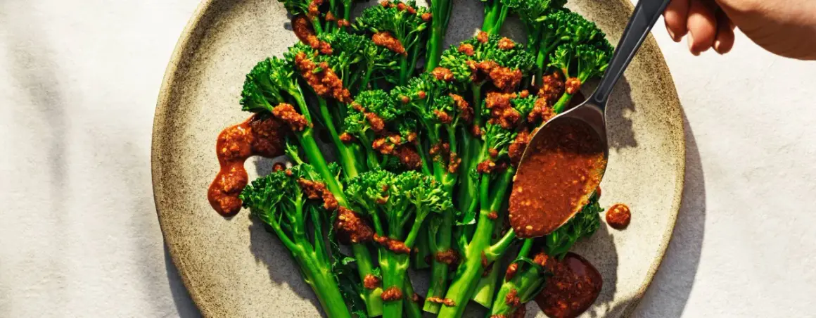 Ånga broccoli med en kryddig sås. En sked häller över mer sås på de gröna buketterna.