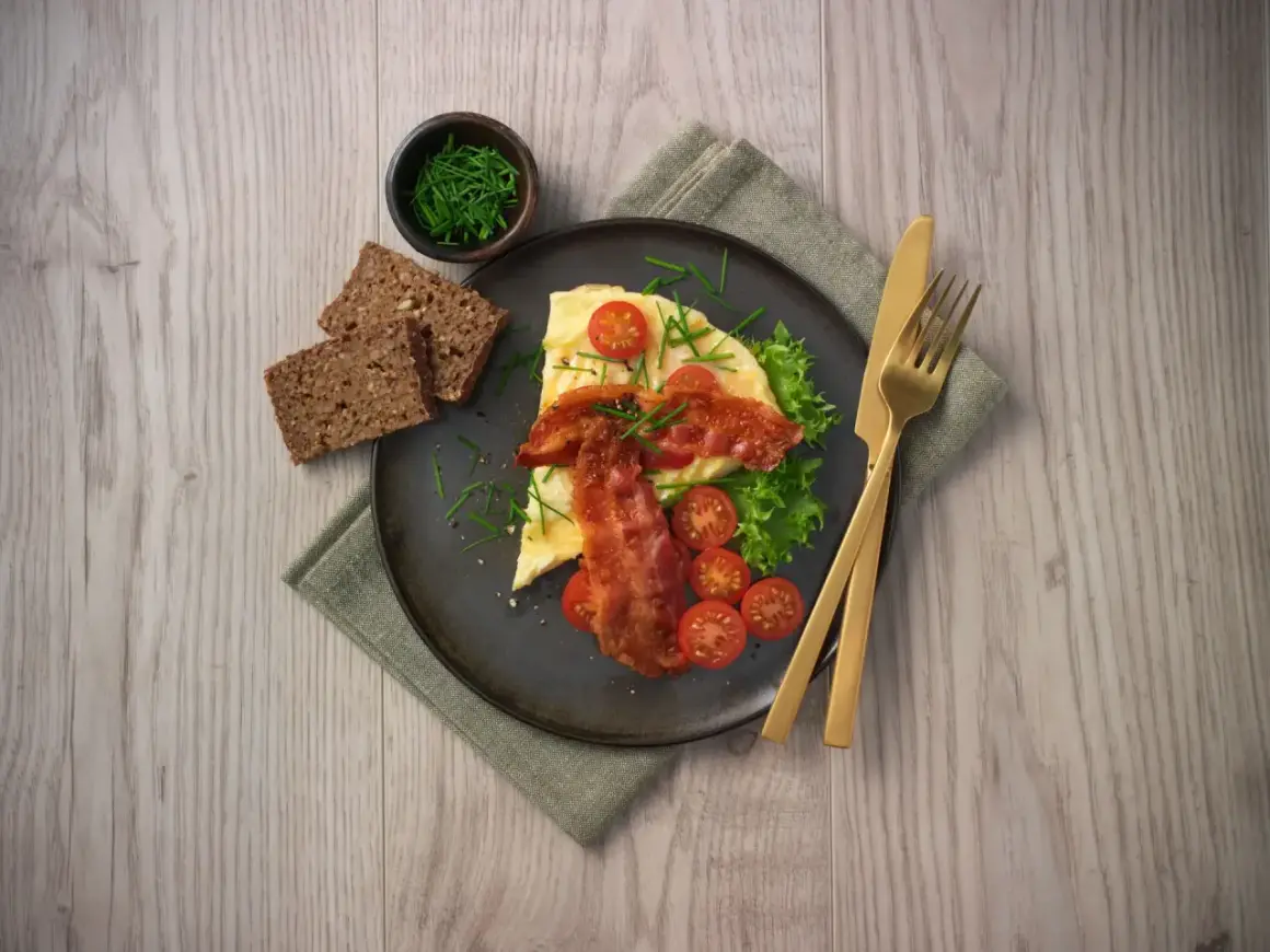 En härlig omelett i ugn med knaperstekt bacon, färska tomater, sallad och grovt bröd. Serveras med gräslök.