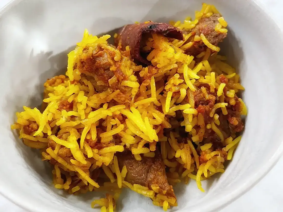 En skål med gyllene ris och möra bitar av lammkött. En härlig lamm biryani som ser otroligt god ut.