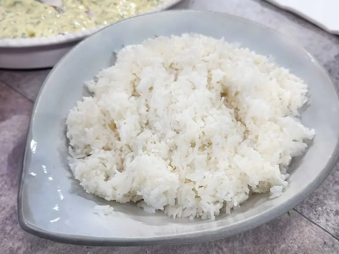 Perfekt fluffigt ris, enkelt att laga mat i riskokare. En skål med vitt ris står framför en annan skål med mat.