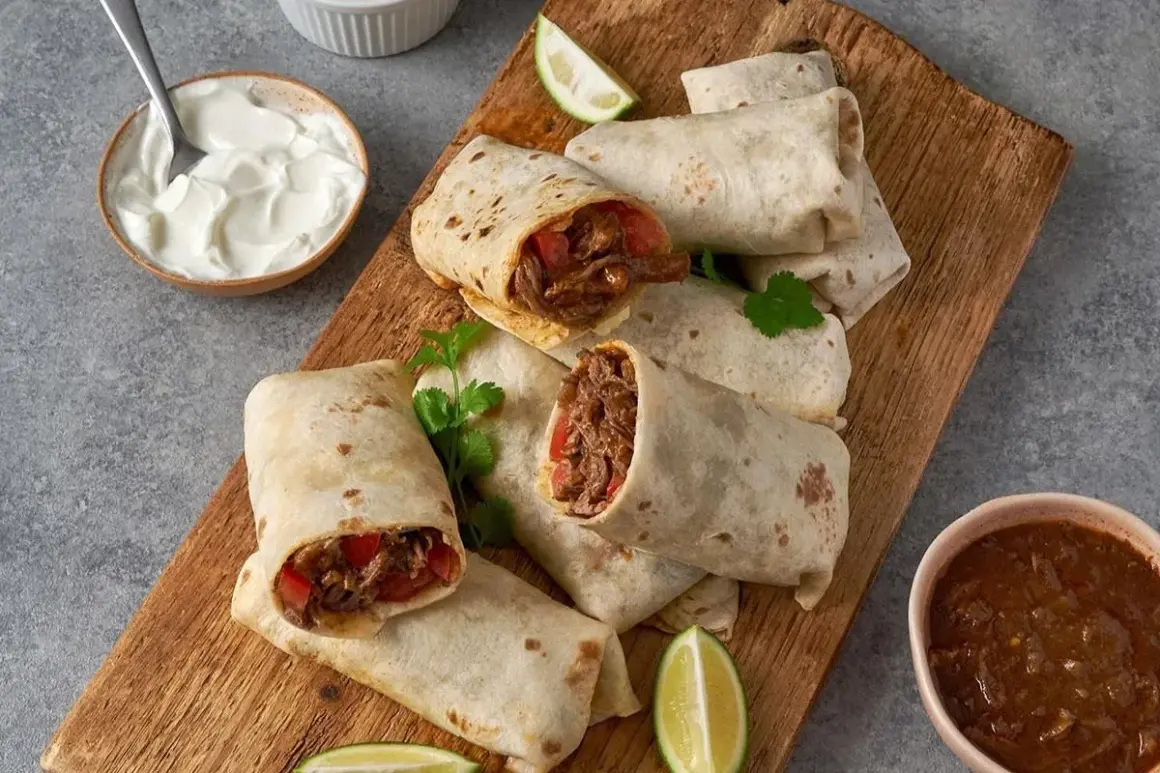 En hög med saftiga chicken burritos på en träskärbräda, serverade med gräddfil, salsa och limeklyftor.