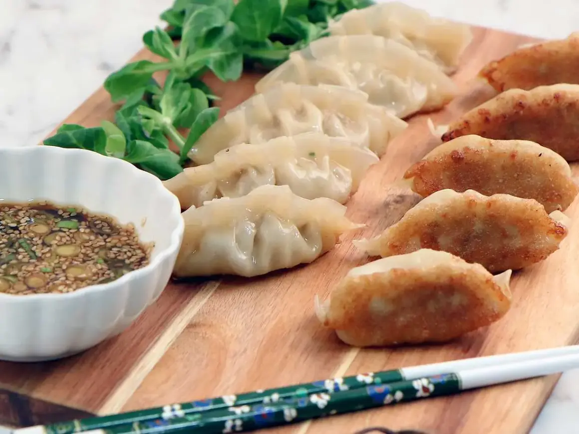 En rad gyllene, stekta dumplings och ångade dumplings serveras med en dippsås och grönsaker. Ett perfekt dumplings recept för en god måltid.