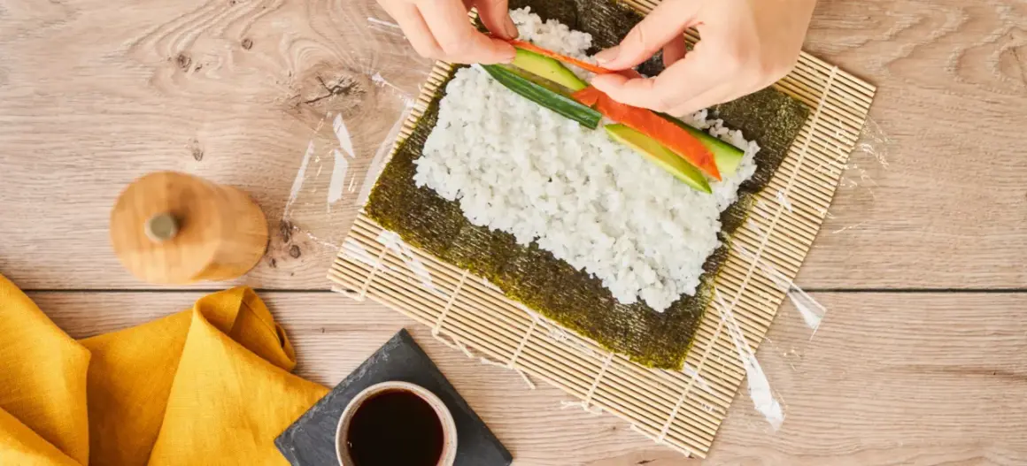 Händer lägger lax och gurka på ris för sushi maki.