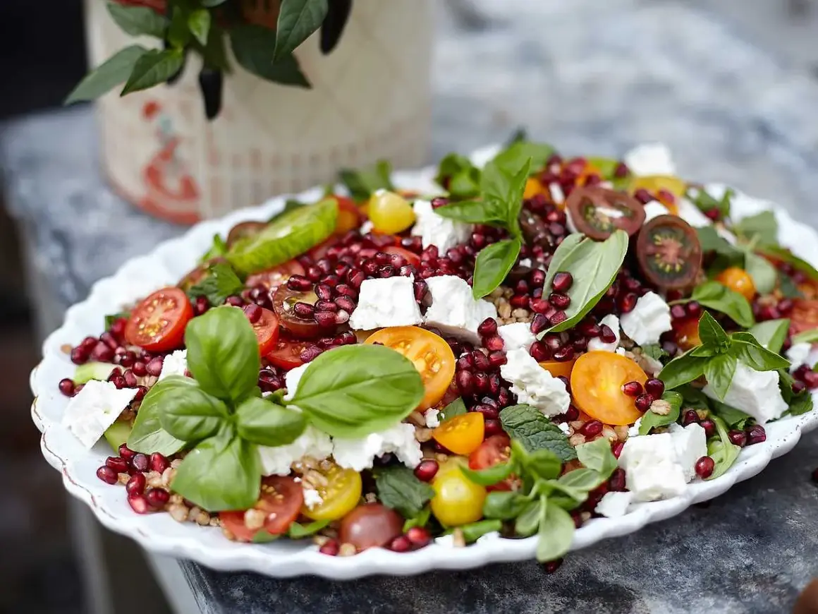 En färgglad coban salata med granatäpple, tomat, gurka, fetaost och basilika på ett vitt fat.