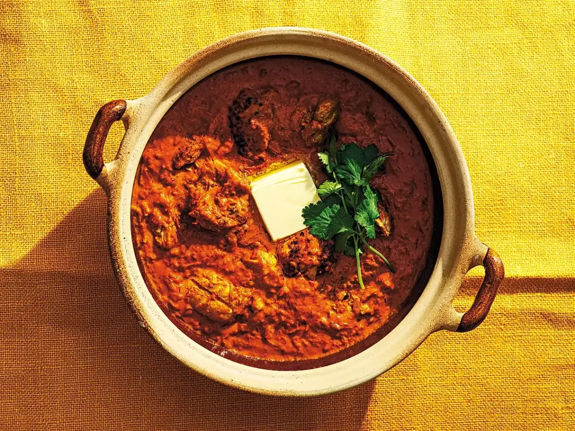 En mustig kycklingrätt i en keramikskål, toppad med en smörbit och koriander. Detta är vad "masala" betyder – en kryddblandning som ger djup och smak.